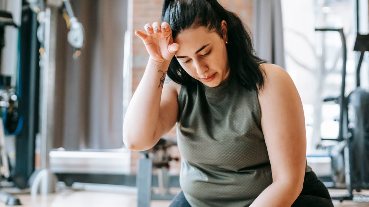 Overweight woman with dark hair in sportswear wiping sweat from face while training in gym in daytime